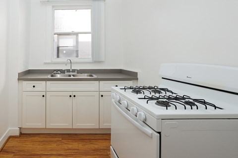 A white gas stove in a kitchen with wooden floors and white cabinets.